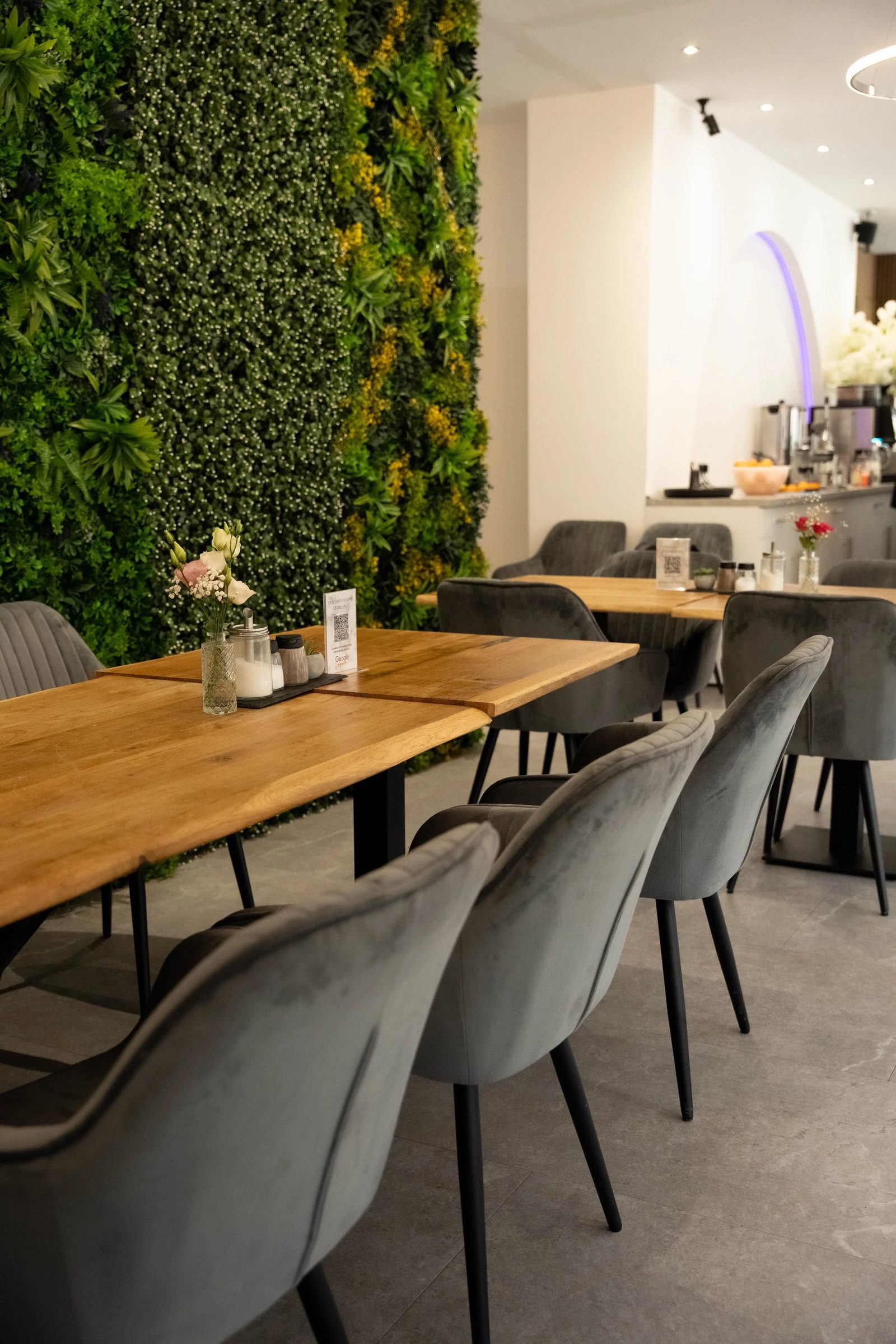 Eichentische und graue Samtsessel vor der grünen Pflanzenwand im Café Renaissance